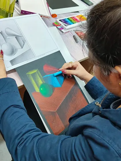 A student practicing object drawing and shading with soft pastels, learning how to represent 3D forms and light sources.
