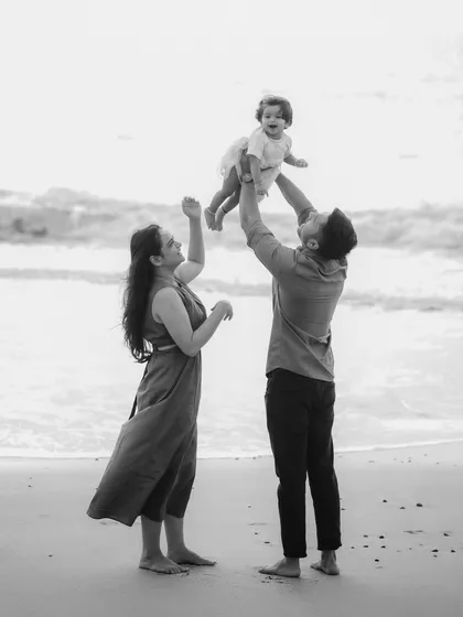 A joyful black and white scene of a father lifting his child up towards the sky on the beach. The composition captures a sense of freedom and fun during a family seaside outing.