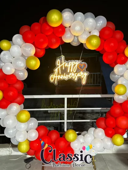 A simple and classic anniversary balloon ring, perfect for a terrace or outdoor party. The red and white balloons are accented with yellow, and a neon sign glows in the center.