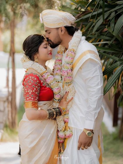 A loving embrace, with the groom kissing the bride's forehead. The couple's traditional attire and the soft background create a classic and elegant wedding portrait.