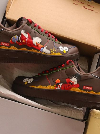 This design is a mashup of two iconic art styles. I hand-painted Kaws-inspired elements alongside the classic cartoon character Scrooge McDuck on a pair of brown Nike Air Force 1 Supreme lows.