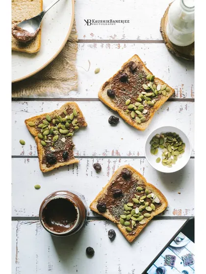 A creative flatlay of chocolate spread on toast, topped with pumpkin seeds. This bright and playful composition is perfect for a breakfast menu or a food blogger's social media feed.