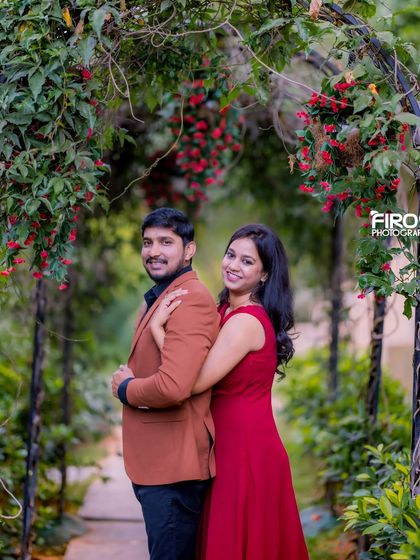 A romantic pose under a floral archway, with the red flowers creating a beautiful and passionate frame.