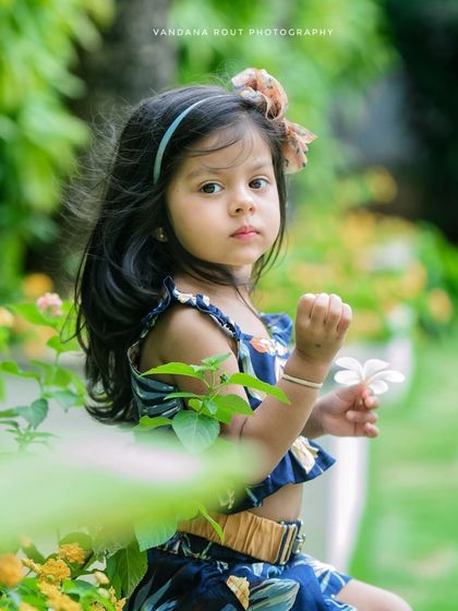 A lovely close-up of a young girl holding a flower. The soft focus on the background makes her stand out, highlighting her sweet and curious expression.