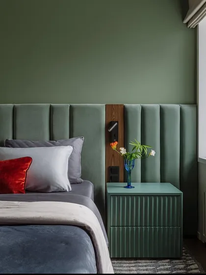 The right color can make all the difference. This bedroom uses a soothing green for the wall and headboard, creating a calm and relaxing environment. The fluted bedside table adds a touch of modern texture.
