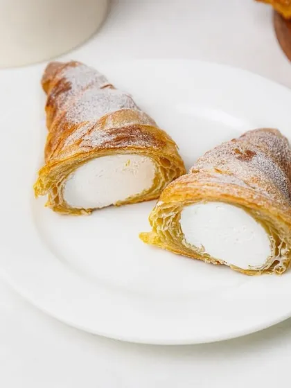 Two cream-filled pastry horns dusted with powdered sugar, presented on a white plate. This image clearly shows the product, making it great for an online bakery catalog.