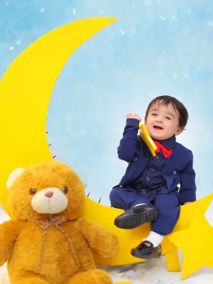 A classic and dreamy baby portrait setup. The combination of the crescent moon prop, a fluffy teddy bear, and a sharp little suit makes for a timeless and adorable photograph.