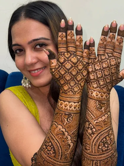 A happy bride showcasing her intricate grid-patterned mehendi that extends up her arms, perfect for her wedding day.