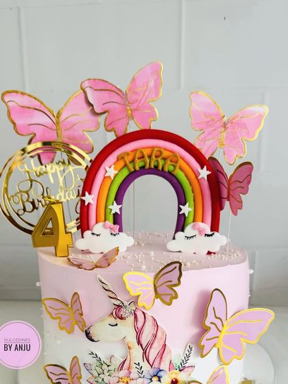 A magical unicorn and rainbow cake, adorned with pink butterflies and a golden "Happy Birthday" topper.