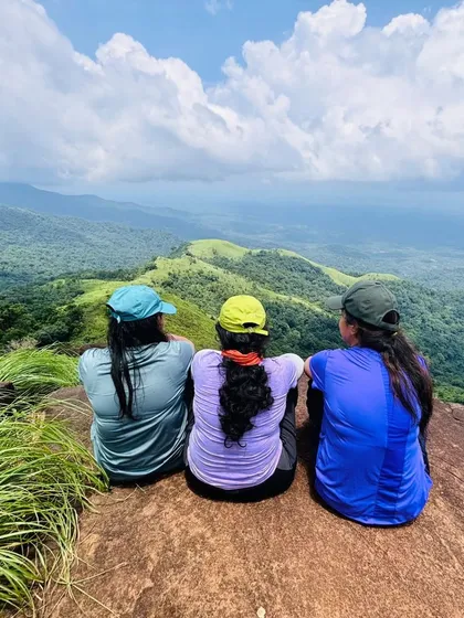 Three friends sitting on a rock, enjoying the panoramic view from the Kurinjal peak.