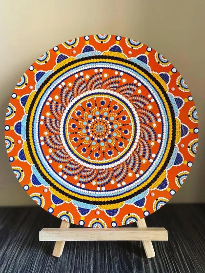 Here is a smaller dot mandala, displayed on an easel to show how it can be a beautiful tabletop decor item. The bright orange and blue design is full of energy and intricate detail.