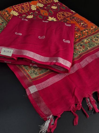 A festive linen cotton dress material. The set includes a multi-colored printed top fabric and a contrasting bright pink dupatta with a silver border and tassels.
