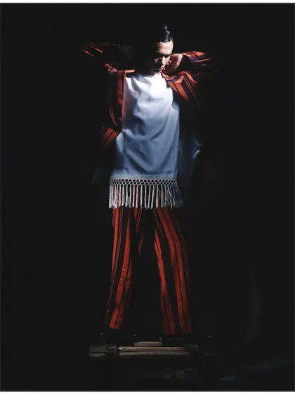 A full-body shot from the 'Silhouette' project, where the model is shrouded in darkness. The lighting carves out the shape of the striped suit and fringed top, focusing entirely on form.
