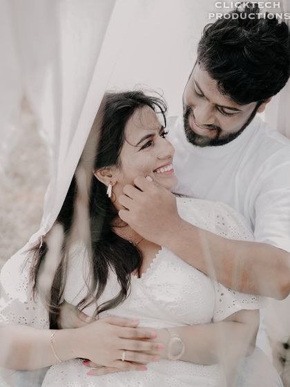 A joyful and intimate moment, with the groom caressing the bride's cheek, both smiling, seen through a soft white fabric.