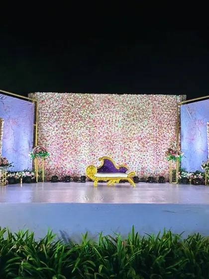 This reception stage combines a full flower wall with modern, artistic panels and a unique gold-and-purple divan, creating a look that is both luxurious and contemporary.