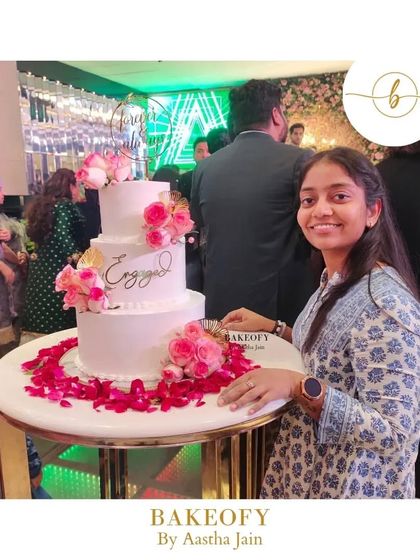 A picture of me with the three-tier engagement cake at the venue. After two years of avoiding large cakes, pulling this off felt like a huge personal victory.