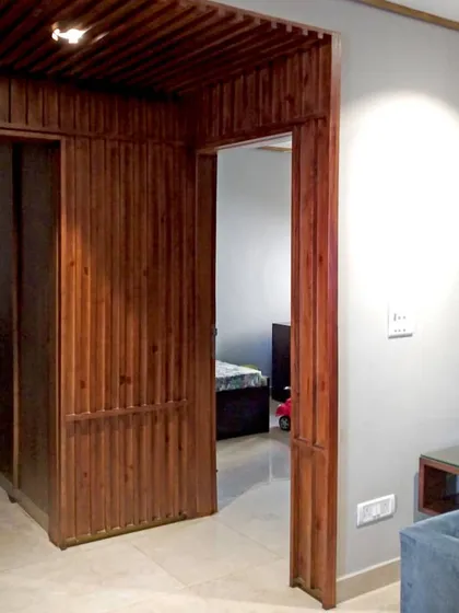 The wooden paneling in the Gurgaon residence extends to create doorways and passages, maintaining a cohesive design language that defines spaces through material and rhythm.