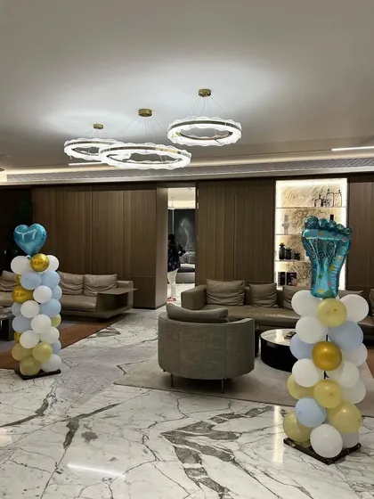 Simple yet elegant balloon pillars in pastel blue, white, and gold, used to decorate the entrance of a baby shower venue.