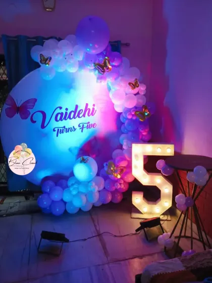 A dreamy butterfly-themed birthday with a custom-printed backdrop, purple-lit balloon garland, and a large marquee number '5'.