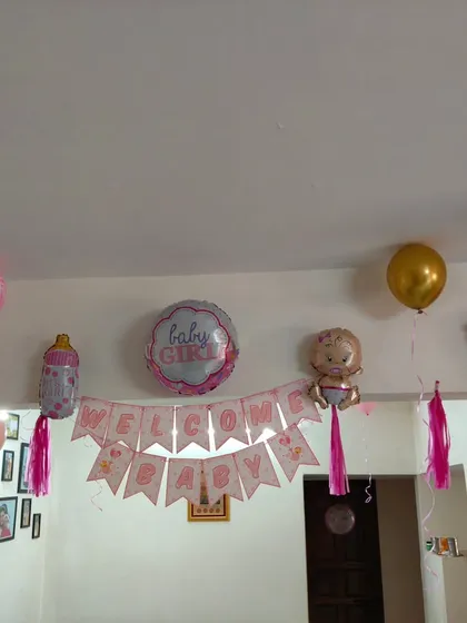 A simple and sweet 'Welcome Baby Girl' home decoration with a banner and themed foil balloons like a baby bottle and foot.