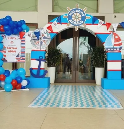 The grand entrance to a sailor-themed party, with a "Welcome Aboard" arch, lighthouse props, and a sea-inspired color palette of red, white, and blue.