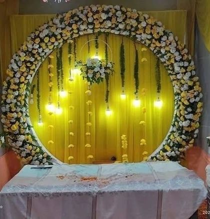 A beautiful circular backdrop for a Haldi ceremony, decorated with yellow and white flowers and hanging lights.