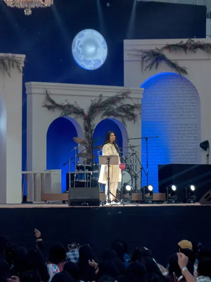 Nayab Midha on the beautifully decorated stage at Spoken'25. Her elegant, natural makeup look complements the ethereal stage design.