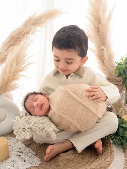I love bringing creative themes to life, like this warm, boho-inspired setup. Here, a proud big brother holds his new sibling, showcasing how I can blend a stylized session with genuine family moments.