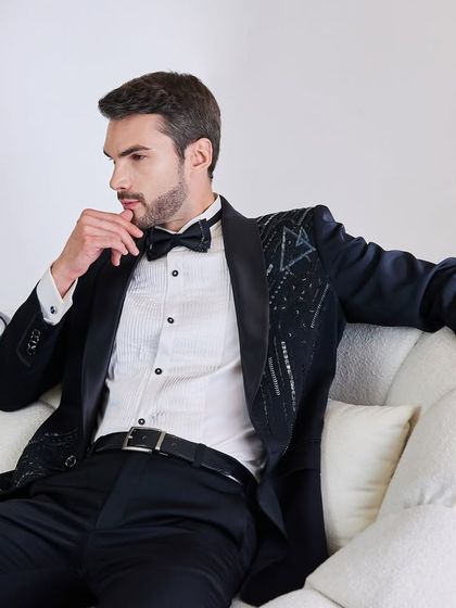 The geometric embellished tuxedo in a relaxed, thoughtful pose. This view shows how the unique detailing on the lapel adds a contemporary touch to a classic silhouette.