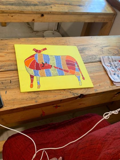 A work-in-progress shot of a colorful, striped Gond cow on a bright yellow canvas. This piece shows the playful and imaginative side of this tribal art form.