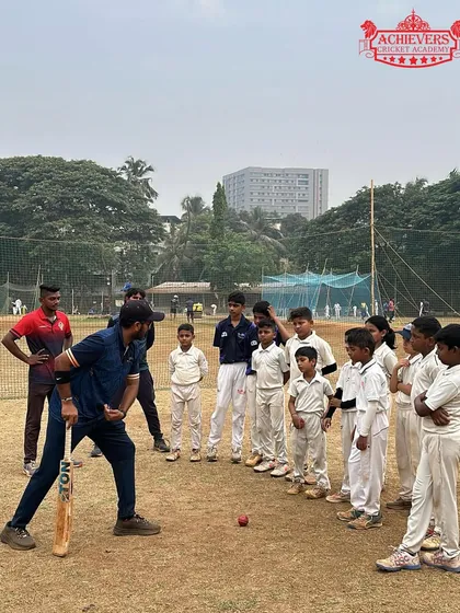 A coach demonstrates the correct batting stance to a group of young, attentive players during our summer camp. Learning from the best, to be the best.
