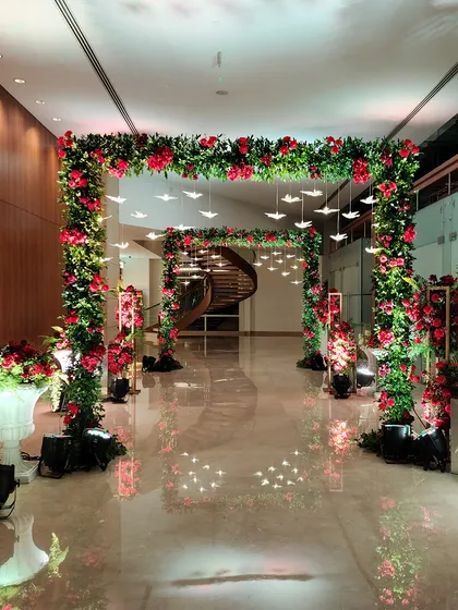 A magnificent square floral arch made of red roses, with delicate illuminated birds hanging from the center. This design creates a stunning frame for the venue's entrance.