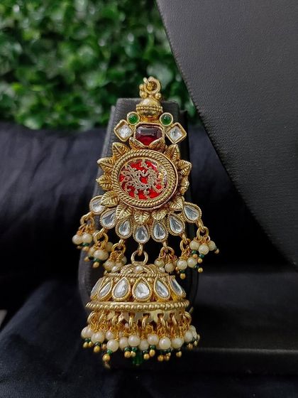 A detailed shot of the matching jhumka earring, showcasing the red pendant and kundan work that ties the whole bridal set together.
