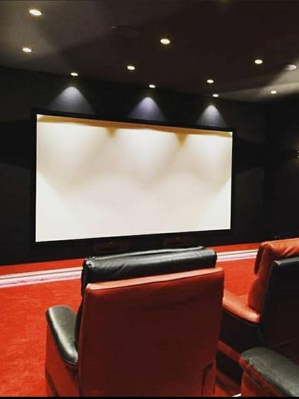 This installation features a classic cinema aesthetic with a bold red and black color scheme. The tiered seating with premium recliners ensures every viewer has a perfect sightline to the screen. The dark walls and ceiling minimize light reflection, maximizing the projector's performance for a true movie theater feel.