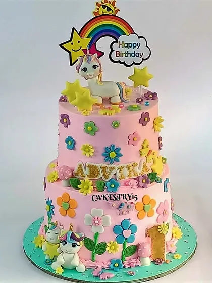 A cheerful two-tier unicorn and rainbow cake. This pink cake is covered in colorful fondant flowers and features cute unicorn figures for a happy first birthday.