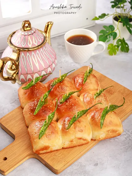 The stuffed pav buns served with tea. The styling with a cute pink teapot creates a cozy, high-tea vibe for this classic Mumbai snack.