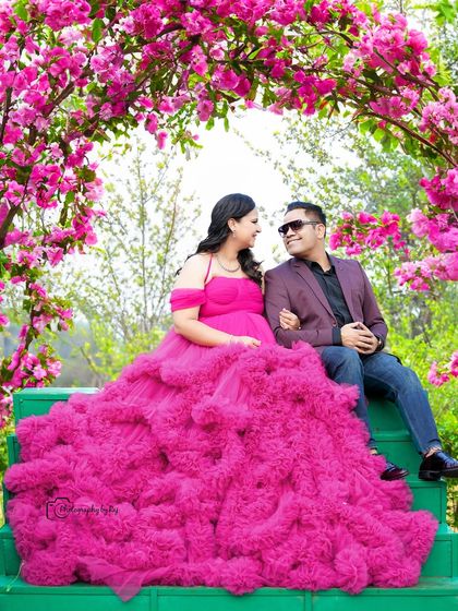 A romantic couple's portrait under a pink floral arch. The voluminous pink gown creates a dramatic and beautiful effect.