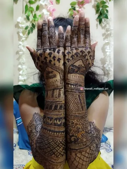 A shy bride or 'navri' peeking through her fully decorated hands. This shows a full-coverage design extending up to the elbows, ready for the wedding day.