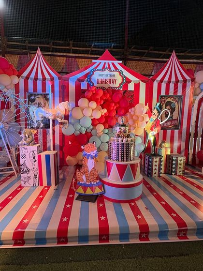 The main stage of a carnival party, featuring a classic red-and-white striped big-top design, a multi-tiered cake, and a tiger prop.