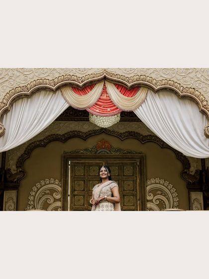 A wide shot showcasing the beautiful bride against the grand, ornate backdrop of her engagement venue.