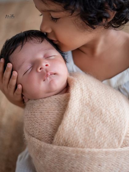 A close-up of a big sister's gentle kiss on her newborn sibling's forehead. A truly priceless moment of love.