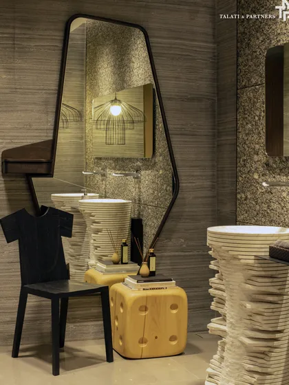This powder bathroom embraces an artistic approach to spatial design. With its quirky blend of elements, including a sculptural stacked-stone basin, an asymmetric mirror, and dramatic lighting, every detail comes together to infuse the space with a sense of spectacle.