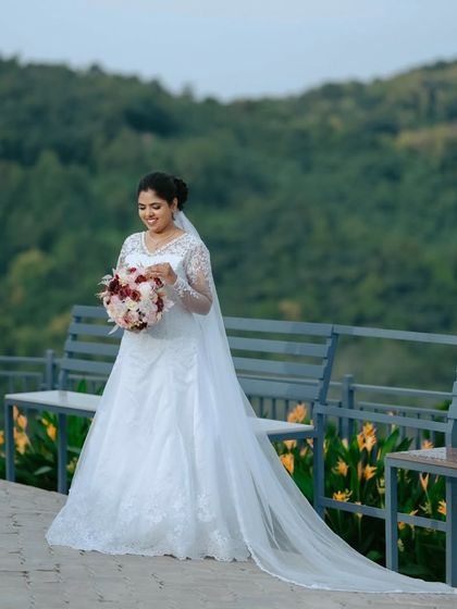 A full-length shot of the bride in her stunning white gown, with the long veil trailing behind her. This portrait highlights the grandeur of the bridal attire against a scenic landscape.
