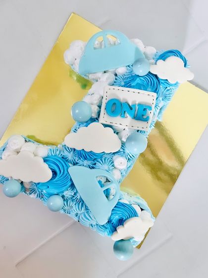 A number one shaped cake for a first birthday. This numeric cake is decorated with blue swirls, fluffy clouds, and little airplane accents for an 'up in the air' theme.