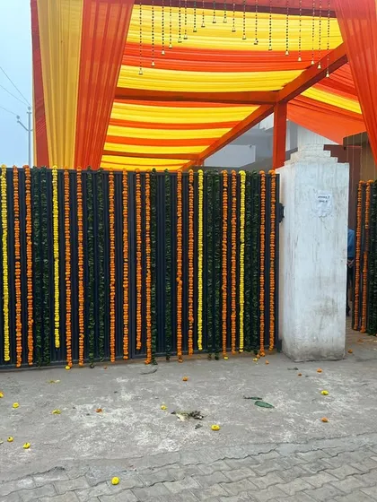 This is an entrance gate decorated with vertical strings of dark green leaves and yellow and orange marigolds. This type of traditional genda phool decoration is a classic choice for home weddings.