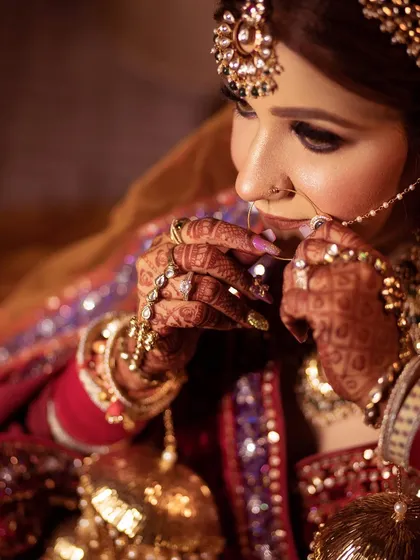 A close-up on the bride's hands as she adjusts her nath, showing off her intricate henna and rings.