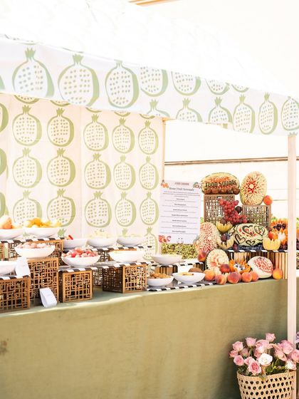 A fruit cart, but make it super cute! For this daytime event, we created a beautiful fruit station with a custom-printed pomegranate canopy and an abundant display of fresh, colorful fruits.