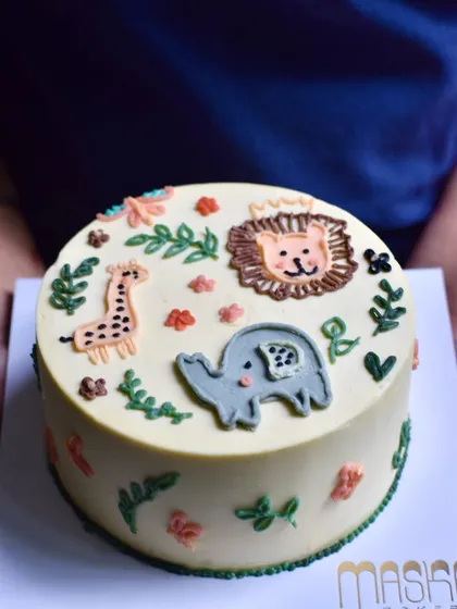 A custom birthday cake for a little animal lover, featuring a hand-piped jungle scene with a friendly lion, giraffe, and elephant. We create whimsical and fun children's birthday cakes using only delicious buttercream, ensuring they taste as good as they look.