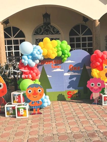 This bright and colorful outdoor setup is based on the Super Simple Songs theme. It features large cutouts of the characters, alphabet blocks, and a cheerful balloon arrangement, perfect for a first birthday party.