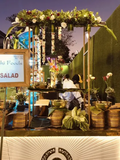 My team setting up a rustic-themed salad bar for an outdoor event, featuring fresh flowers, hanging decorations, and a variety of salad bowls.